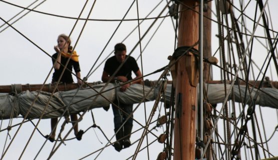 Nő és férfi vitorláshajó árbócára másztak