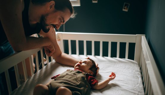 férfi kiságyban fekvő baba fölé hajol