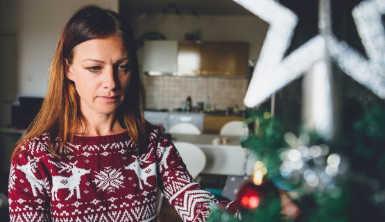 karácsonyfa mellett álló szomorú arcú nő