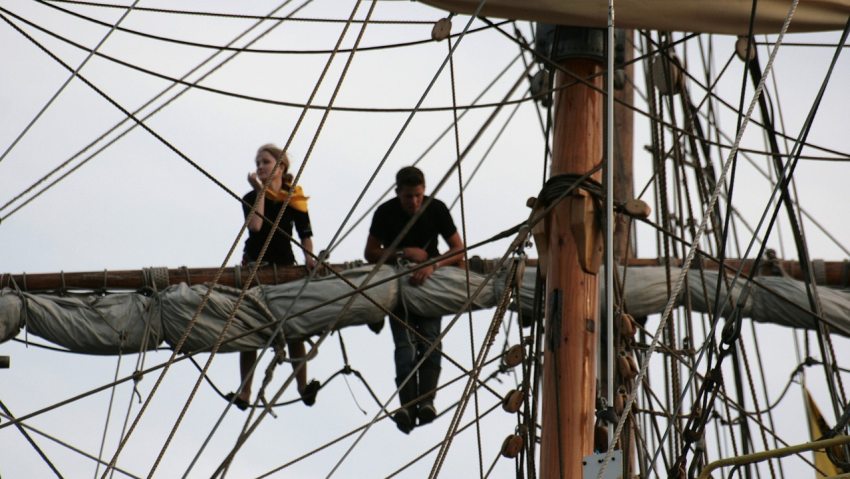 Nő és férfi vitorláshajó árbócára másztak