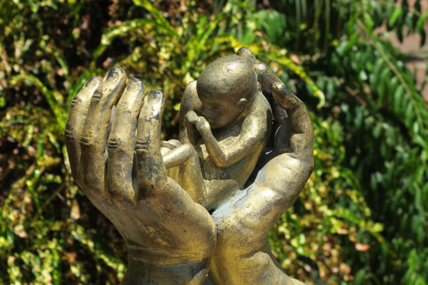 kéz alakú szobor, ami kisbabát tart