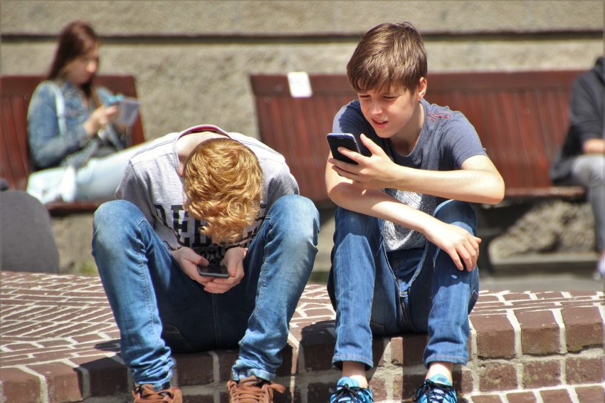 két fiú ül egy lépcsőn, telefonját nézve