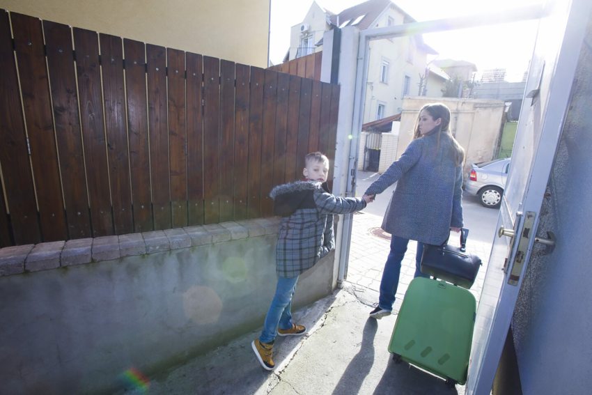 bőrönddel utcára lépő nő és gyermek