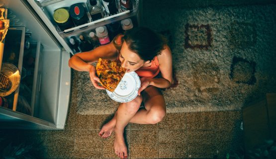 Anonim túlevő lány pizzát eszik a nyitott hűtőajtó előtt