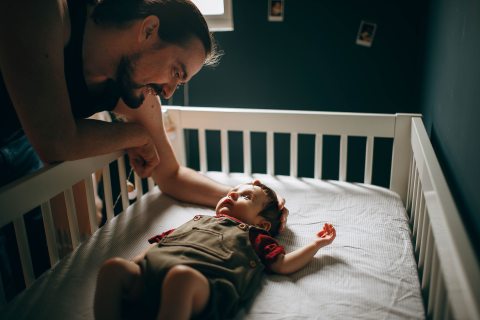 férfi kiságyban fekvő baba fölé hajol