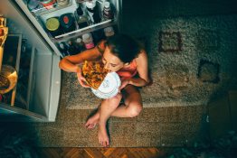 Anonim túlevő lány pizzát eszik a nyitott hűtőajtó előtt